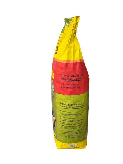Seitenansicht eines gelb-rot-grünen Beutels Profagus Buchen Grill-Holzkohle, 'DER SOMMER HIT'. Sichtbar sind Teile der Vorderseite sowie die Seitenwand mit Texten wie 'Brennt schnell ab', 'Glüht lang und hell' und Abschnitten zur Nachhaltigkeit, darunter 'Nachhaltigkeit ist unser Anspruch. Seit über 125 Jahren!'.